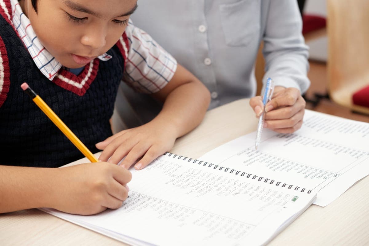 Student writing English composition in notebook with tutor guidance